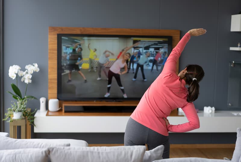 Senior woman following an online stretching class looking at TV screen