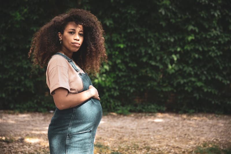 Pregnant-afro-hair-woman-in-the-city-posing-in-front-of-a-beautiful-green-wall-of-plants
