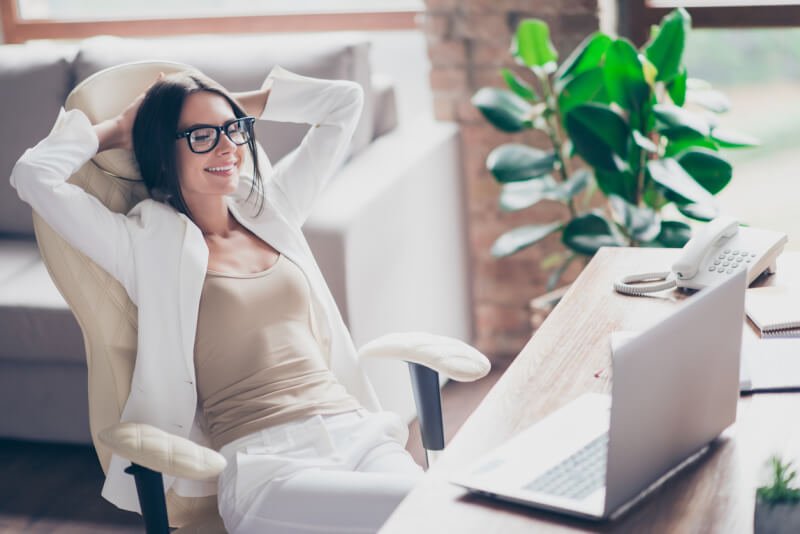 woman in white suit, glasses sitting on chair at her desk in office, holding arms behind the head with close eyes